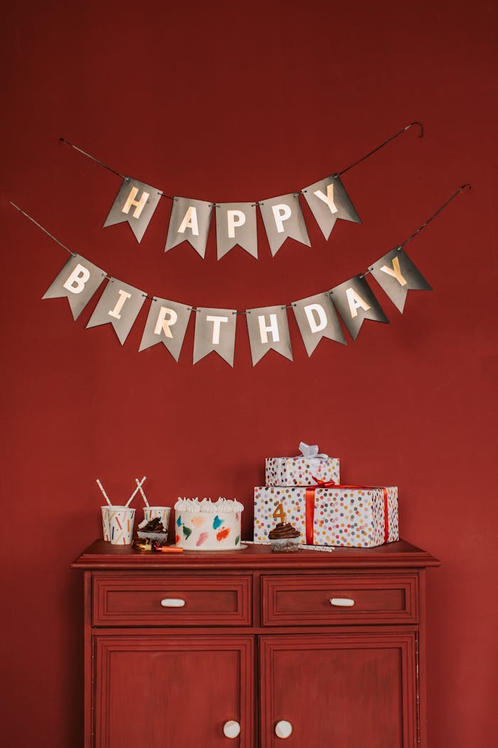 Decorative happy birthday banner with festive gifts and cake on a red cabinet.
