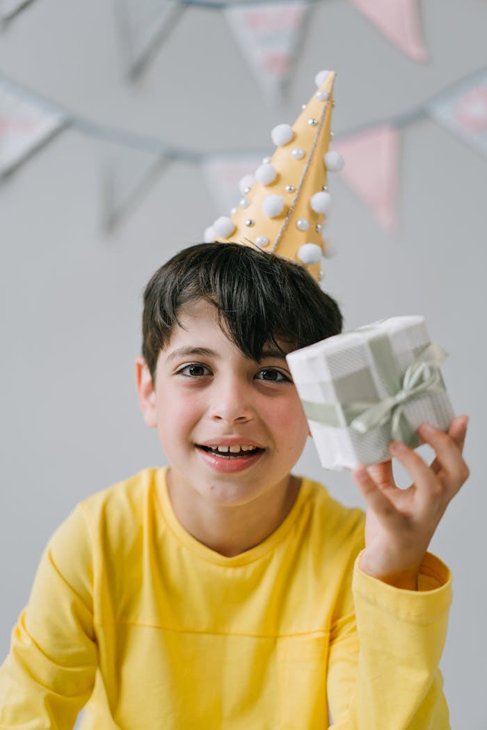 Excited boy in a party hat holding a wrapped gift, celebrating his birthday with joy.